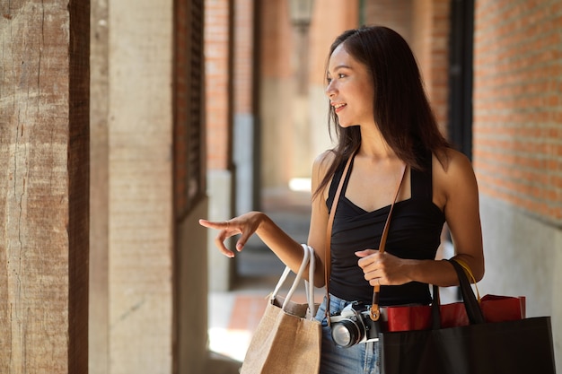 Glückliche junge asiatische Frau genießen Solo-Shopping und Reisen mit Einkaufstüten auf der Suche nach Laden
