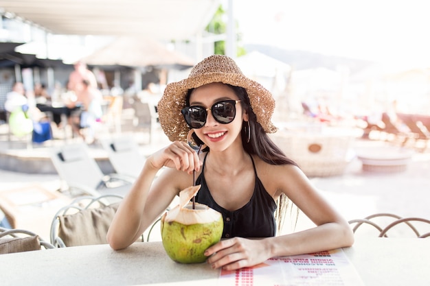 Glückliche junge asiatische Frau genießt Kokosnussgetränk in der Strandbar, Provinz Phuket, Thailand