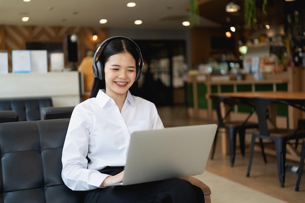Glückliche junge asiatische Frau lächelt mit Laptop beim Sitzen im Café. Junge asiatische Frau, die in einem Café und in einer Videoanrufkonferenz auf einem Laptop sitzt.
