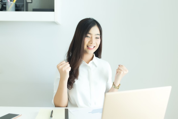 Glückliche junge asiatische Geschäftsfrau beendete ihre Arbeit am Arbeitsplatz.