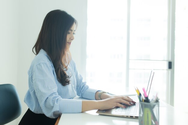 Glückliche junge asiatische Geschäftsfrau, die an ihrem Laptop am Arbeitsplatz arbeitet.