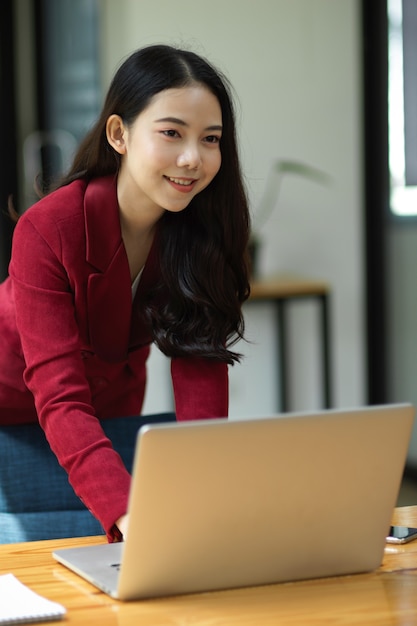 Glückliche junge asiatische Geschäftsfrau, die Laptop-Computer verwendet, um ihr neues Projekt zu entwickeln und zu erforschen