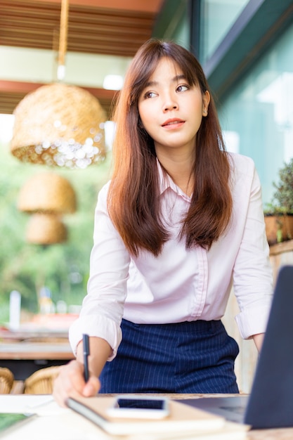 Glückliche junge attraktive asiatische stehende Geschäftsfrau beim Arbeiten an ihrem Computer an einem Patio im Freien außerhalb ihres Büros