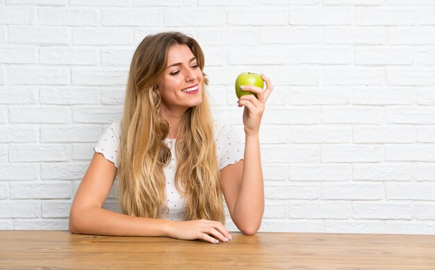 Glückliche junge blonde Frau mit einem Apfel