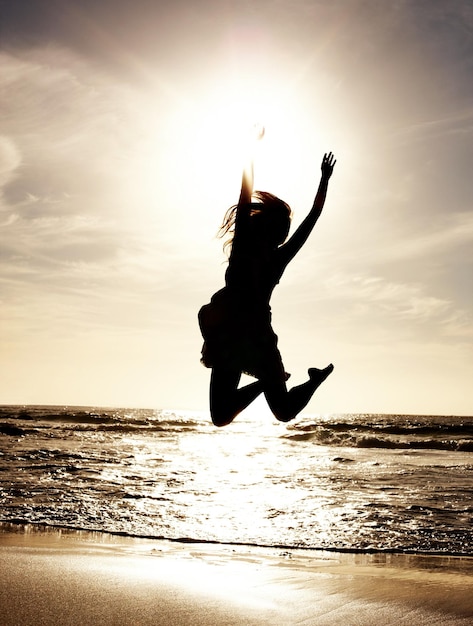 Glückliche junge Dame, die am Strand springt Porträt einer hübschen jungen Dame, die am Meeresufer im Freien springt