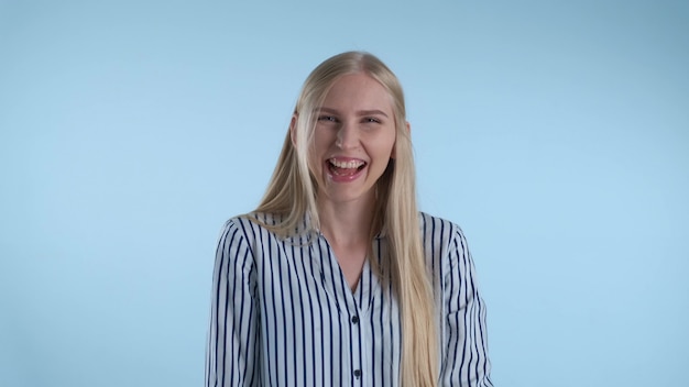 Glückliche junge Dame, die im Lachen auf blauem Hintergrund platzt