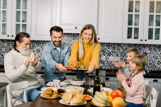 glückliche junge Eltern, Frau und Mann, die Familie, Kindern und Großvater Brathähnchen anbieten und zu Hause eine Dinnerparty veranstalten