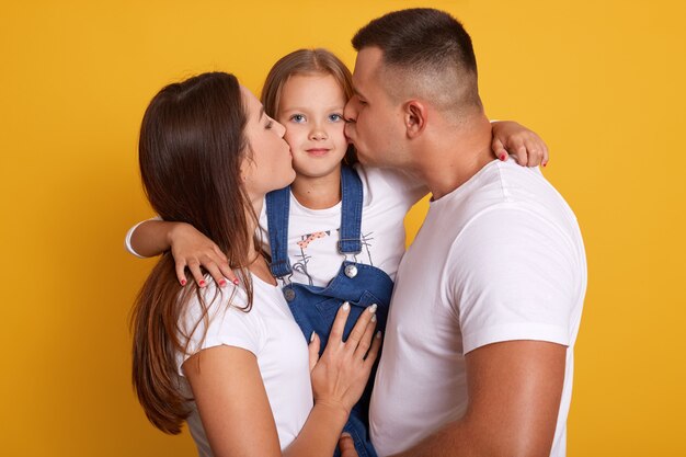 Glückliche junge Familie, die ihre kleine charmante Tochter küsst.