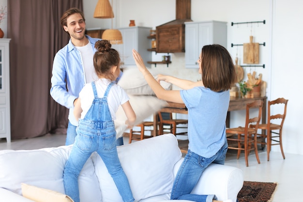 Glückliche junge Familie, die Spaß mit Kissen auf dem Sofa hat.