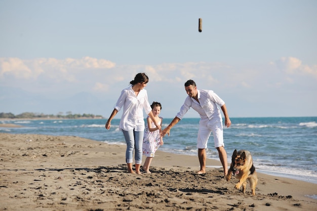 glückliche junge familie in weißer kleidung hat spaß und spielt mit einem schönen hund im urlaub am schönen strand