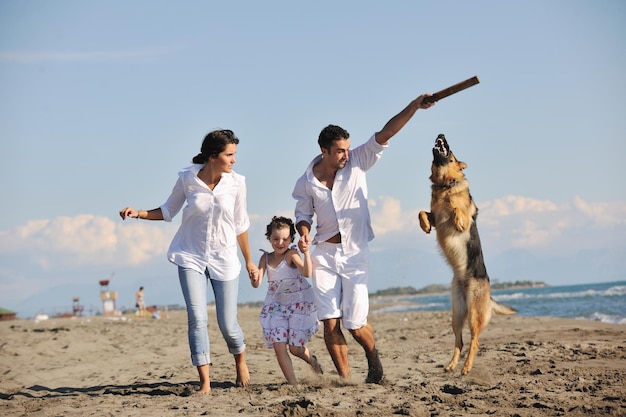 glückliche junge familie in weißer kleidung hat spaß und spielt mit einem schönen hund im urlaub am schönen strand