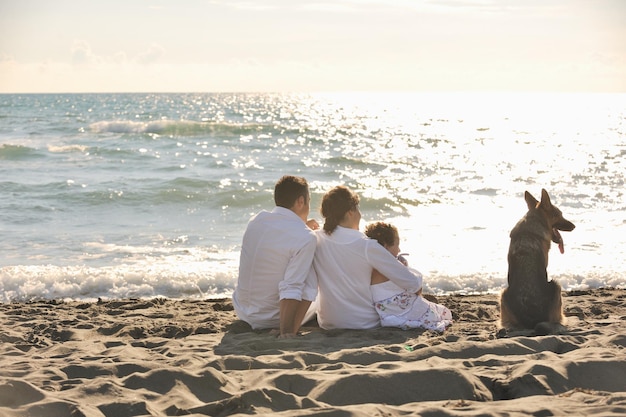 glückliche junge familie in weißer kleidung hat spaß und spielt mit einem schönen hund im urlaub am schönen strand