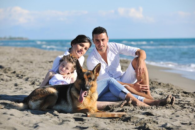 glückliche junge familie in weißer kleidung hat spaß und spielt mit einem schönen hund im urlaub am schönen strand