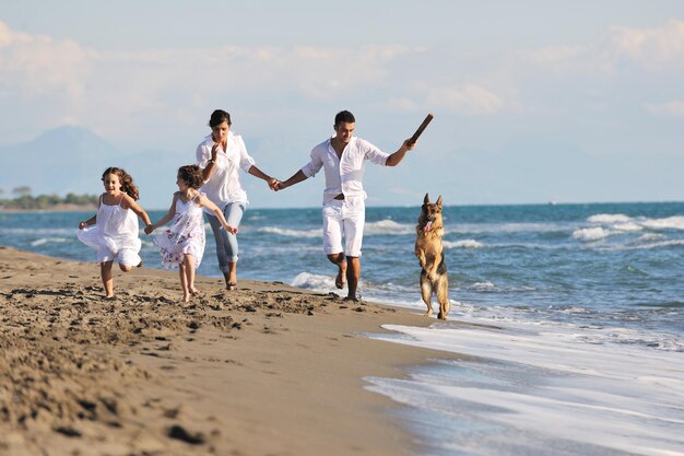 glückliche junge familie in weißer kleidung hat spaß und spielt mit einem schönen hund im urlaub am schönen strand