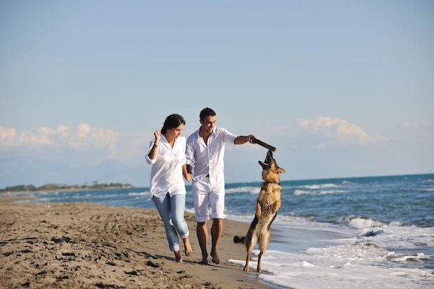 glückliche junge familie in weißer kleidung hat spaß und spielt mit einem schönen hund im urlaub am schönen strand