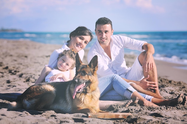 glückliche junge familie in weißer kleidung hat spaß und spielt mit schönem hund im urlaub am schönen strand