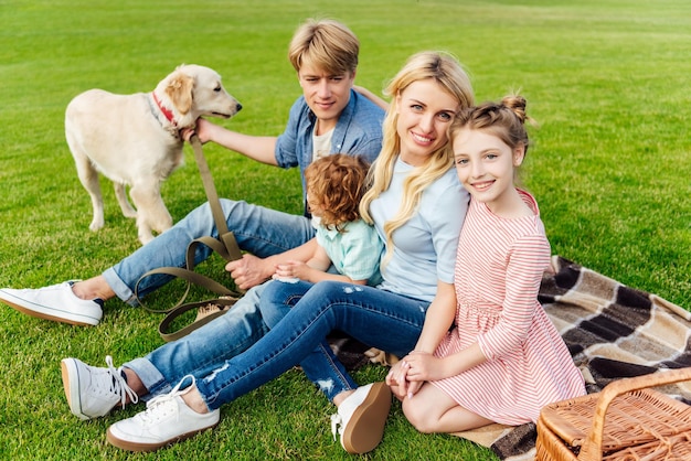 glückliche junge familie mit golden retriever-hund, der auf plaid beim picknick sitzt