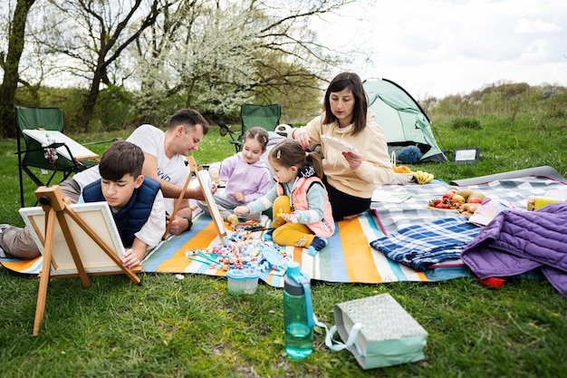 Glückliche junge Familie mit vier Kindern, die Spaß haben und draußen auf der Picknickdecke genießen