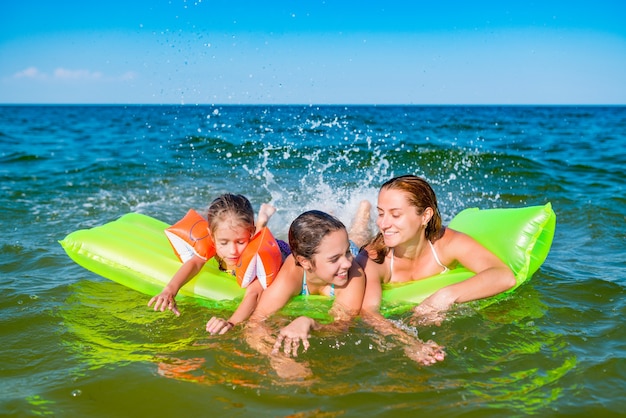 Glückliche junge Familie positive Mutter und zwei kleine Töchter schwimmen auf einer gelben Luftmatratze im Meer an einem sonnigen Sommertag während der Ferien