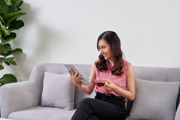Glückliche junge Frau, die auf Sofa sitzt und Tablet-PC im Büro benutzt