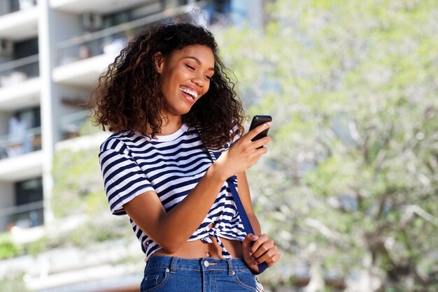 Glückliche junge Frau, die draußen mit Mobiltelefon lächelt