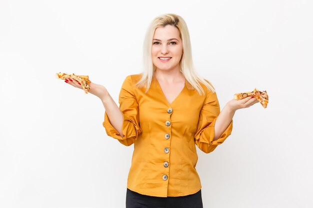 Glückliche junge Frau, die ein Stück heiße Pizza isst, isoliert auf weiß