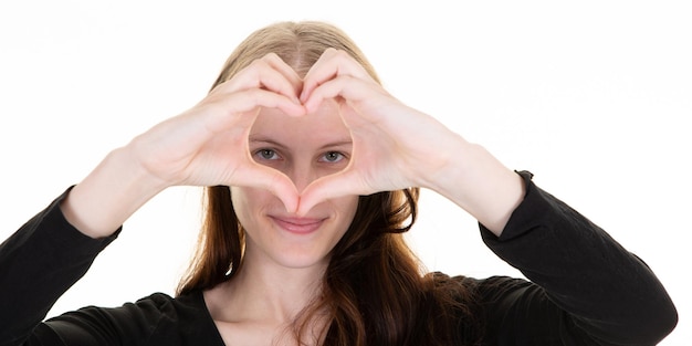 Glückliche junge Frau, die Finger zeigt, liebt Herzzeichen, Augen, Gesicht mit der Hand