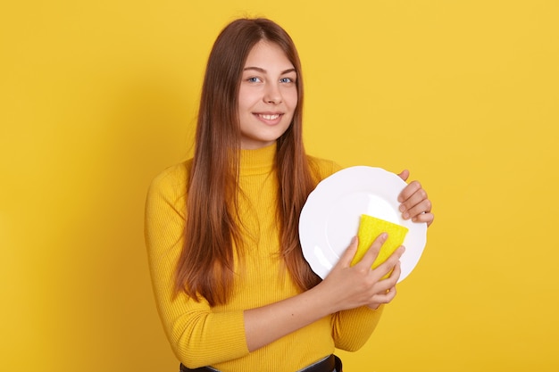 Glückliche junge Frau, die Geschirr spült, lokalisiert auf Gelb