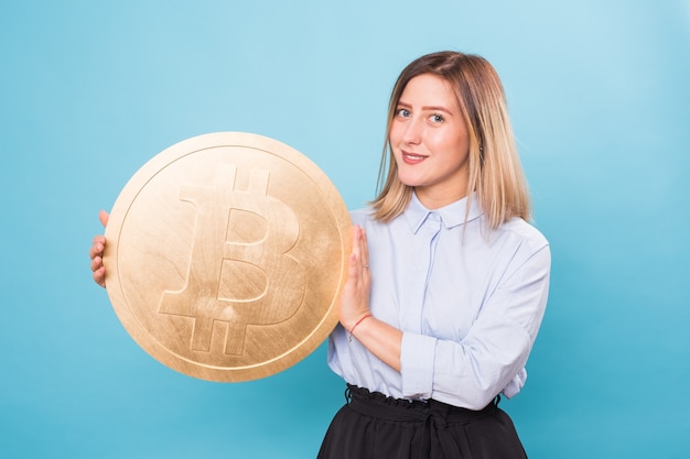 Glückliche junge Frau, die goldene Bitcoin hält, zwinkert und an Kryptowährung denkt.