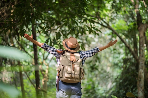 glückliche junge Frau, die ihre Arme anhebt, um die Sonne am Wald zu grüßen