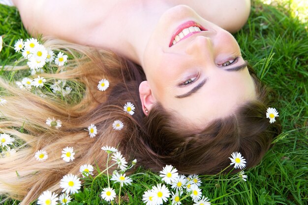 Glückliche junge Frau, die im Park mit Blumen lächelt