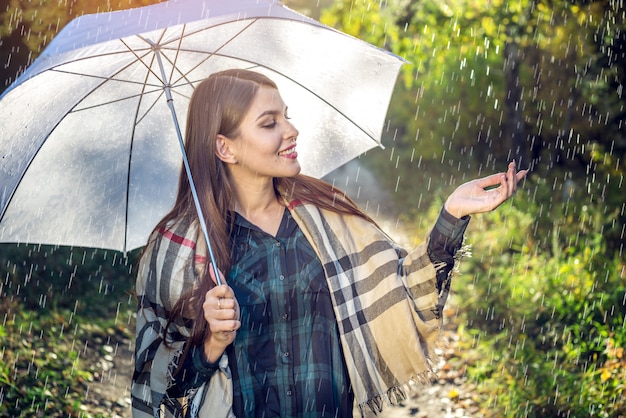 Glückliche junge Frau, die in Sunny Park mit einem weißen Regenschirm im Regen geht