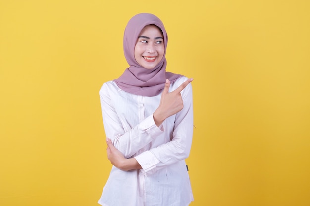 Glückliche junge Frau, die mit ihrem Finger auf die rechte Seite zeigt und Hijab trägt