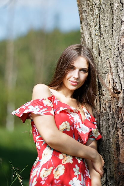 Glückliche junge Frau, die nahe Baum im Sommer steht