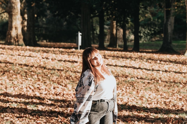 Glückliche junge Frau, die Spaß im Herbstwald hat. Frauenporträt. Glückliches Mädchen in weißem Hemd und Blue Jeans spielt mit Blatt, schaut in die Kamera und lächelt. Platz kopieren. Porträt im Herbstpark.