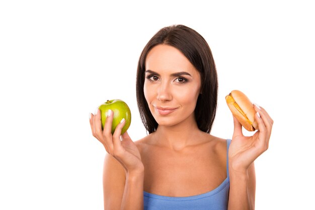 Glückliche junge Frau, die zwischen einem Apfel und einem Burger entscheidet