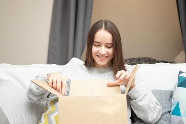 Glückliche junge Frau hat eine Paketbestellung erhalten, packt eine Kiste zu Hause aus