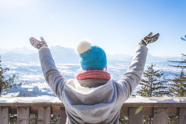 Glückliche junge Frau hebt ihre Hände auf dem Berg und genießt den Blick über die Salzburger Winterzeit auf Gaisberg Salzburg Österreich