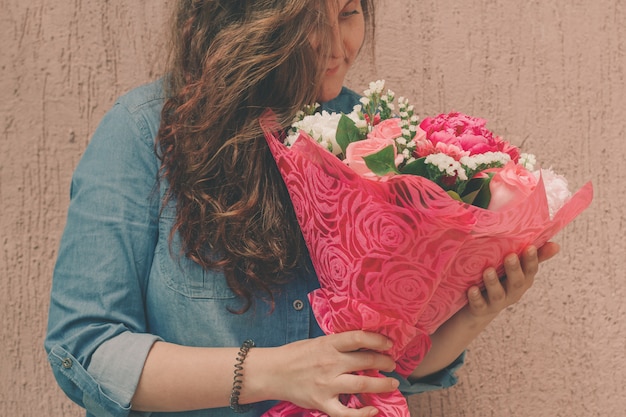 Glückliche junge Frau im Denimkleid mit Blumenstrauß von leichten frischen Blumen
