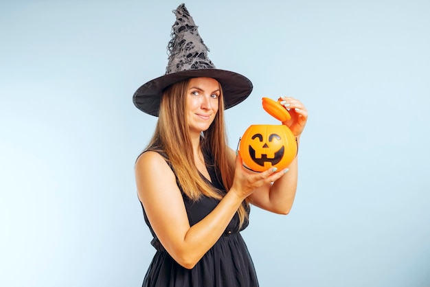 Glückliche junge Frau im Halloween-Hexenkostüm mit Kürbiskorb-Jackolantern