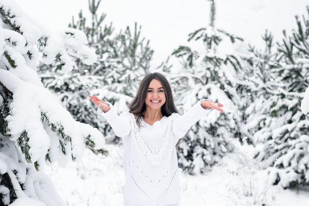 Glückliche junge Frau im schneebedeckten Wald des Winters wirft oben ihren Handschnee.