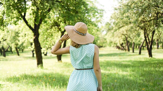 Glückliche junge Frau im Strohhut im sonnigen Garten