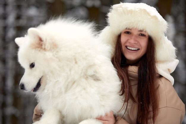 Glückliche junge Frau im Winter hält in ihren Armen und spielt im Schnee mit ihrem Hund