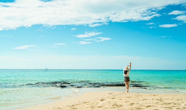 Glückliche junge Frau in den weißen Hemden und in den kurzen Hosen, die am Sandstrand gehen. Entspannen und Urlaub am tropischen Paradiesstrand genießen. Mädchen in den Sommerferien. Sommergefühl. Glücklicher Tag.