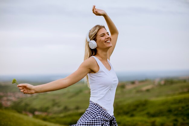 Glückliche junge Frau in der Natur, die Musik auf Kopfhörern hört