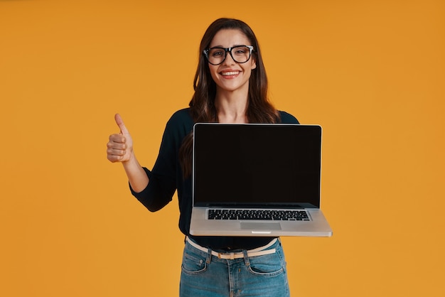 Glückliche junge Frau in intelligenter Freizeitkleidung, die Kopienraum auf Laptop zeigt