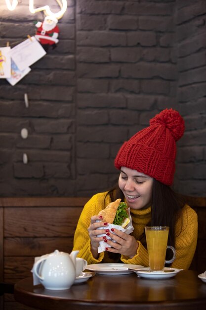 glückliche junge Frau in rotem Winterkleid sitzt in einem Café und trinkt warmen Tee zu Weihnachten