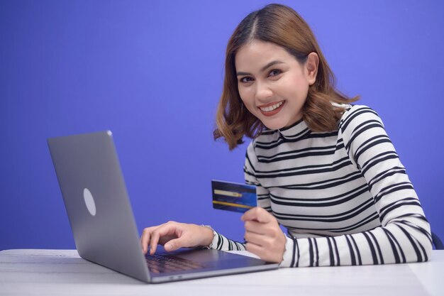 Glückliche junge Frau kauft online per Laptop ein und hält eine Kreditkarte in der Hand