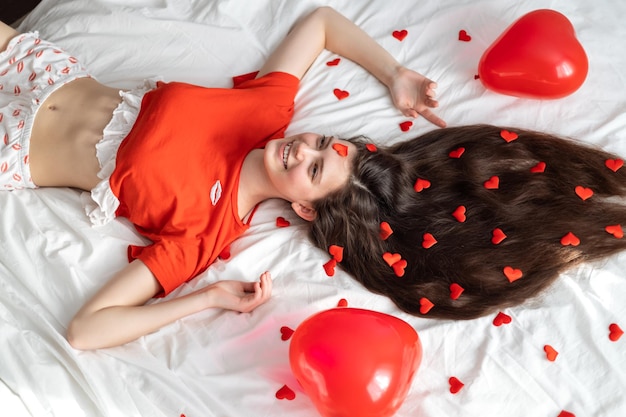 Foto glückliche junge frau liegt auf dem bett mit roten kleinen herzen im haar valentinstag