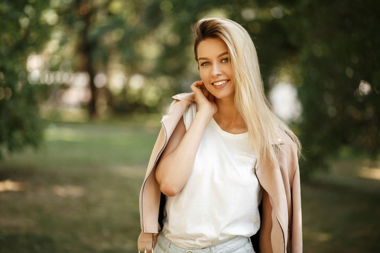 Foto glückliche junge frau mit einem lächeln in einer mode rosa jacke, die im park aufwirft